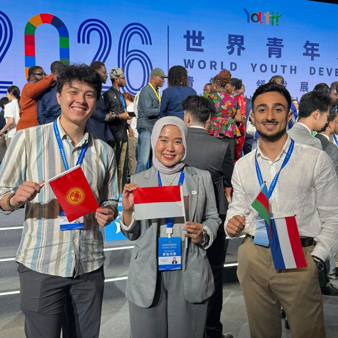 Three young delegates holding the flags of Kyrgyzstan, Indonesia and another nation at the 2026 World Youth Development Forum.